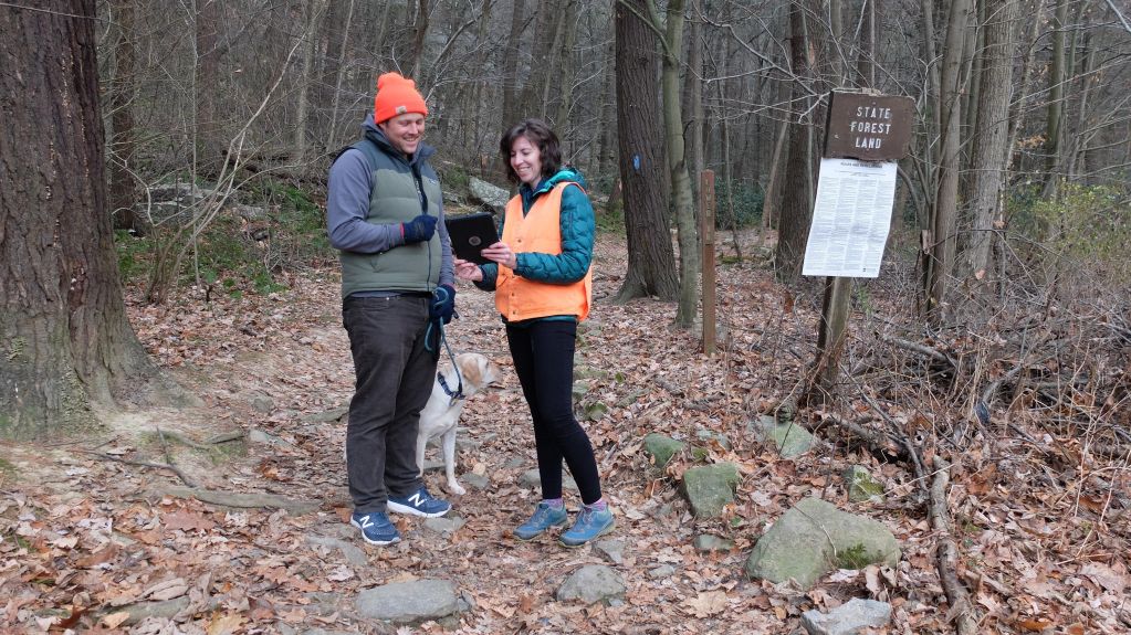 Scientists, including grad student Jamie Peeler, standing in a forest and looking at an iPad