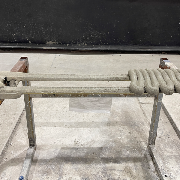 A printed prototype using the current version of the custom extrusion system for in-place 3D concrete printing. This iteration demonstrates the successful integration of continuous reinforcement with concrete deposition, marking a key step in the ongoing development toward structural-scale applications. Credit: Ali Baghi. All Rights Reserved.
