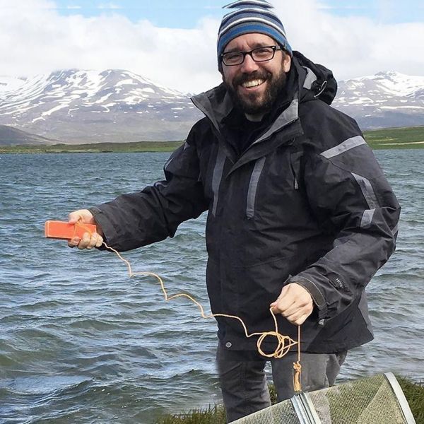 Jason Keagy, assistant research professor of wildlife behavioral ecology, is shown on the bank of an Icelandic lake holding a fish trap during a collection of threespined sticklebacks in a previous study. Credit: Janette Boughman. All Rights Reserved.